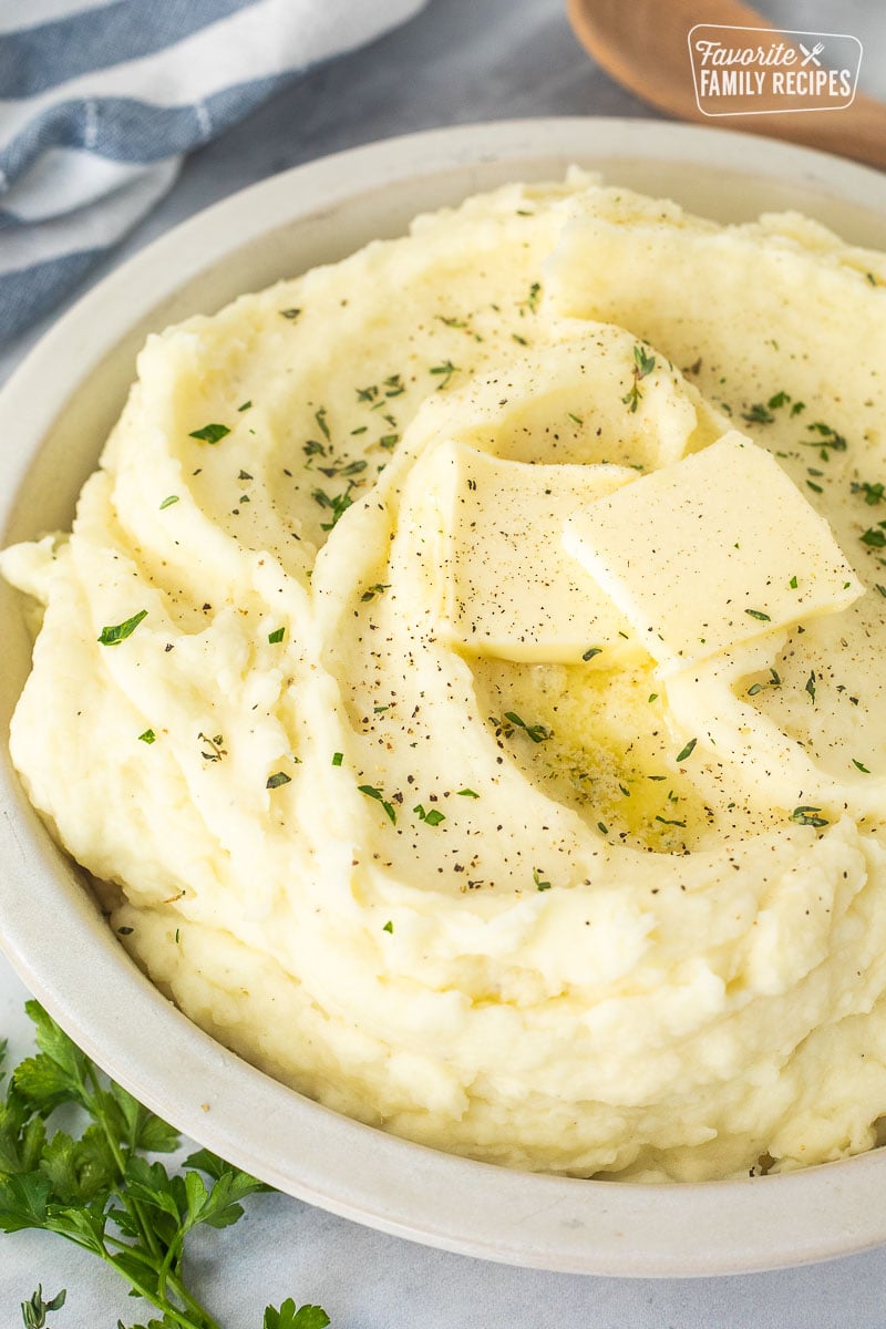 Bowl of homemade mashed potatoes with fresh herbs, pepper, and butter.