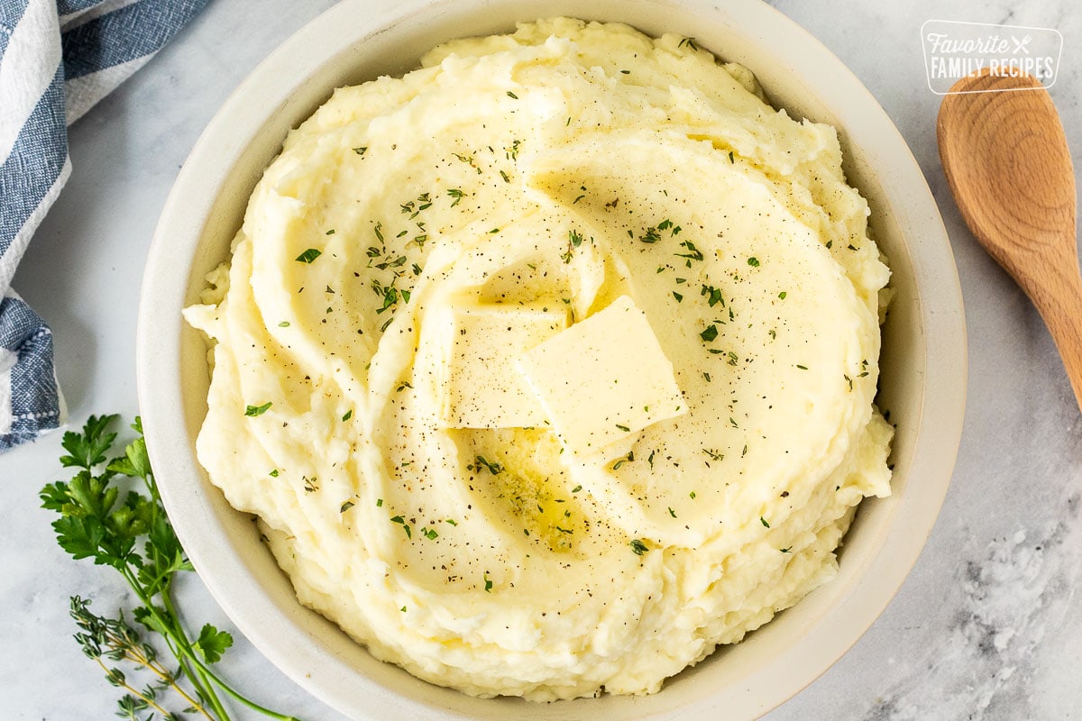 Bowl of mashed potatoes with fresh herbs, pepper, and butter.