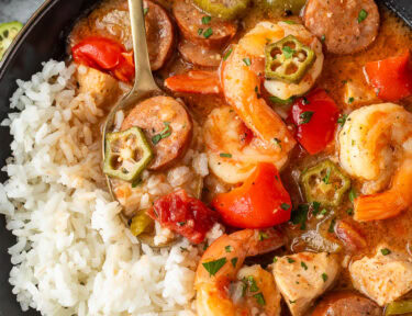 Bowl filled with Instant Pot Gumbo with chicken, shrimp, andouille sausage, and vegetables with white rice on the side.