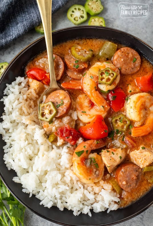 Bowl filled with Instant Pot Gumbo with chicken, shrimp, andouille sausage, and vegetables with white rice on the side.