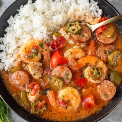 Instant Pot gumbo with shrimp, sausage, chicken, peppers, and other ingredients served in a dish with a bed of rice on the side.