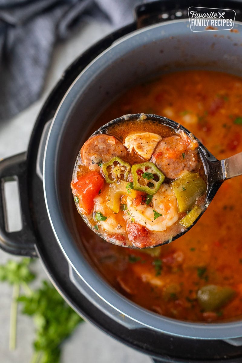 Instant Pot Gumbo with andouille sausage, chicken, shrimp, okra, and vegetables in a serving spoon above an Instant Pot.