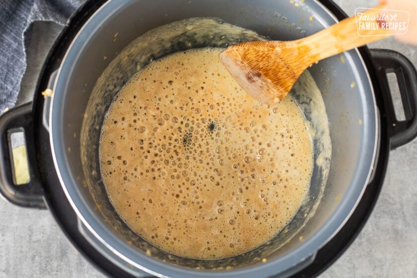 Instant pot with a roux boiling and a wooden spoon.