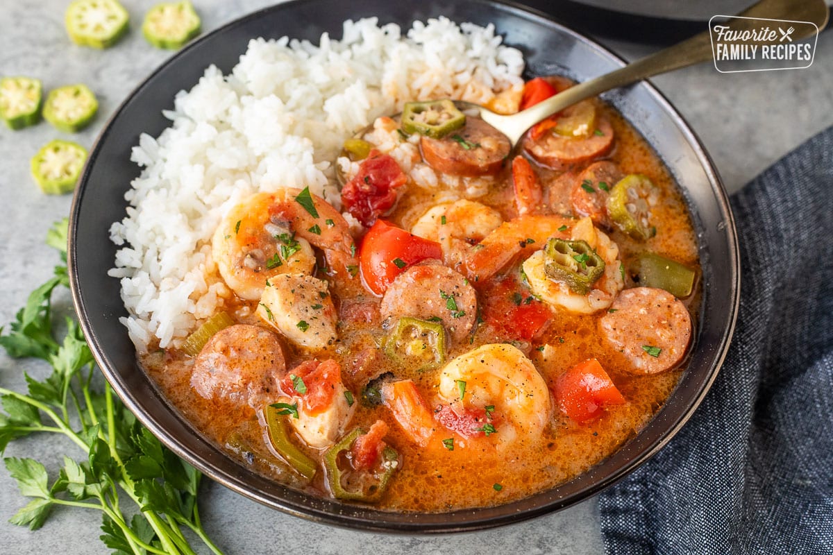 Instant pot gumbo next to a bed of rice with a serving spoon in the gumbo.