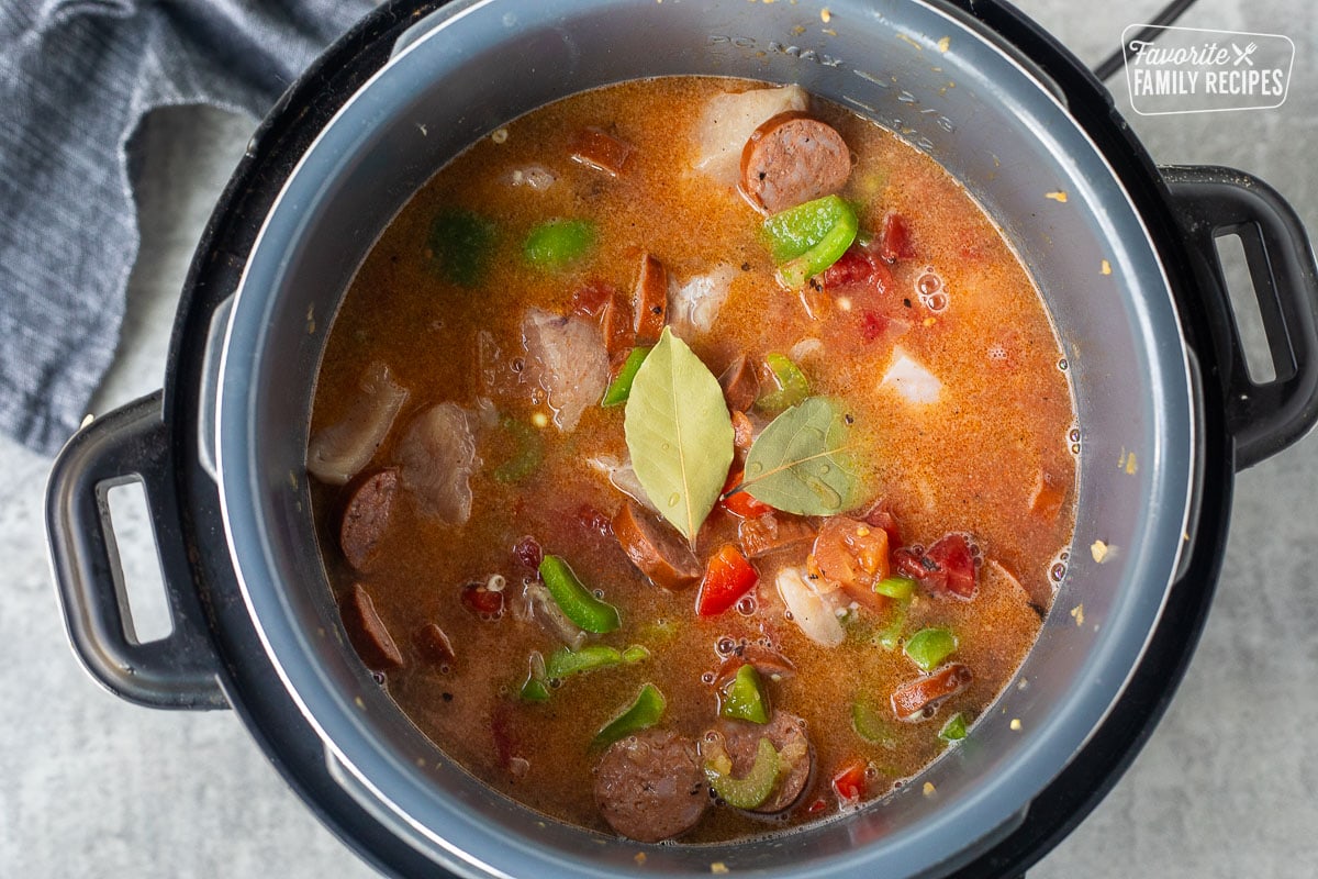 Bay leaves added to instant pot of gumbo with chicken broth, sausage, chicken and peppers.