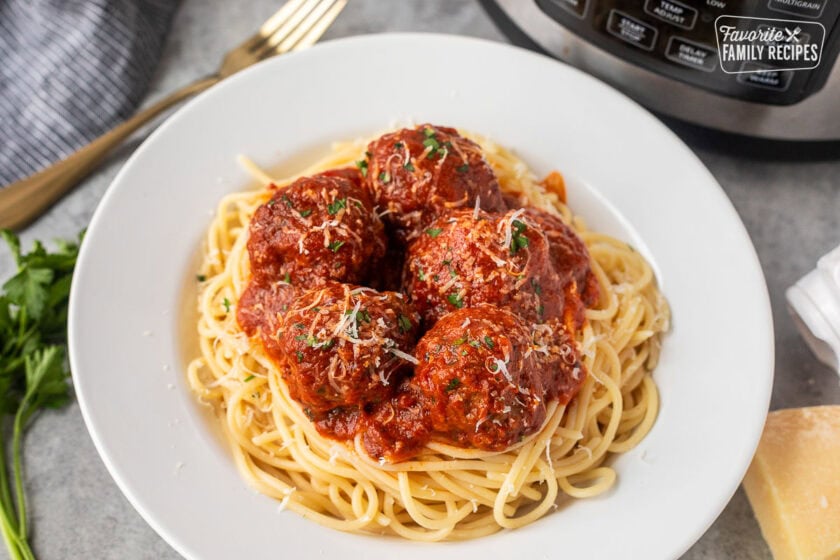 Plate of instant pot meatballs over spaghetti noodles topped with grated Parmesan cheese and fresh parsley.