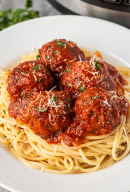 Plate of instant pot meatballs over spaghetti noodles topped with grated Parmesan cheese and fresh parsley.