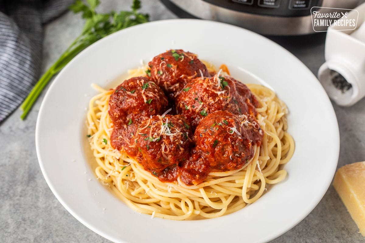 Plate of instant pot meatballs over spaghetti noodles topped with grated Parmesan cheese and fresh parsley.