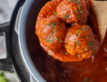 Wooden spoon holding up three instant pot meatballs.