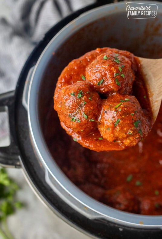 Wooden spoon holding up three instant pot meatballs.