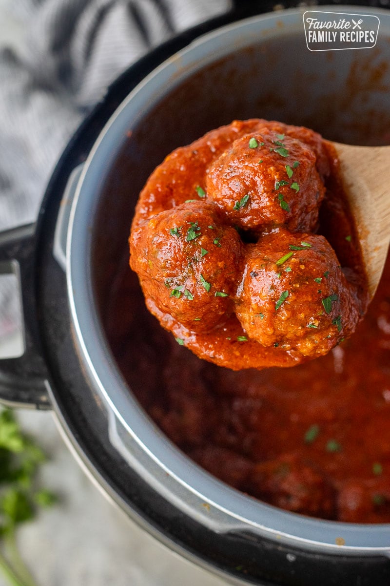 Wooden spoon holding up three instant pot meatballs.