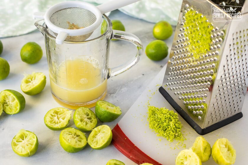 A box grater with zested and juiced limes next to it in preparation to make a key lime pie recipe.