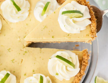 A slice of key lime pie being removed from the full pie