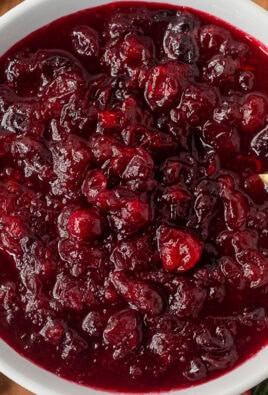 Large glass bowl of orange cranberry sauce with a spoon.