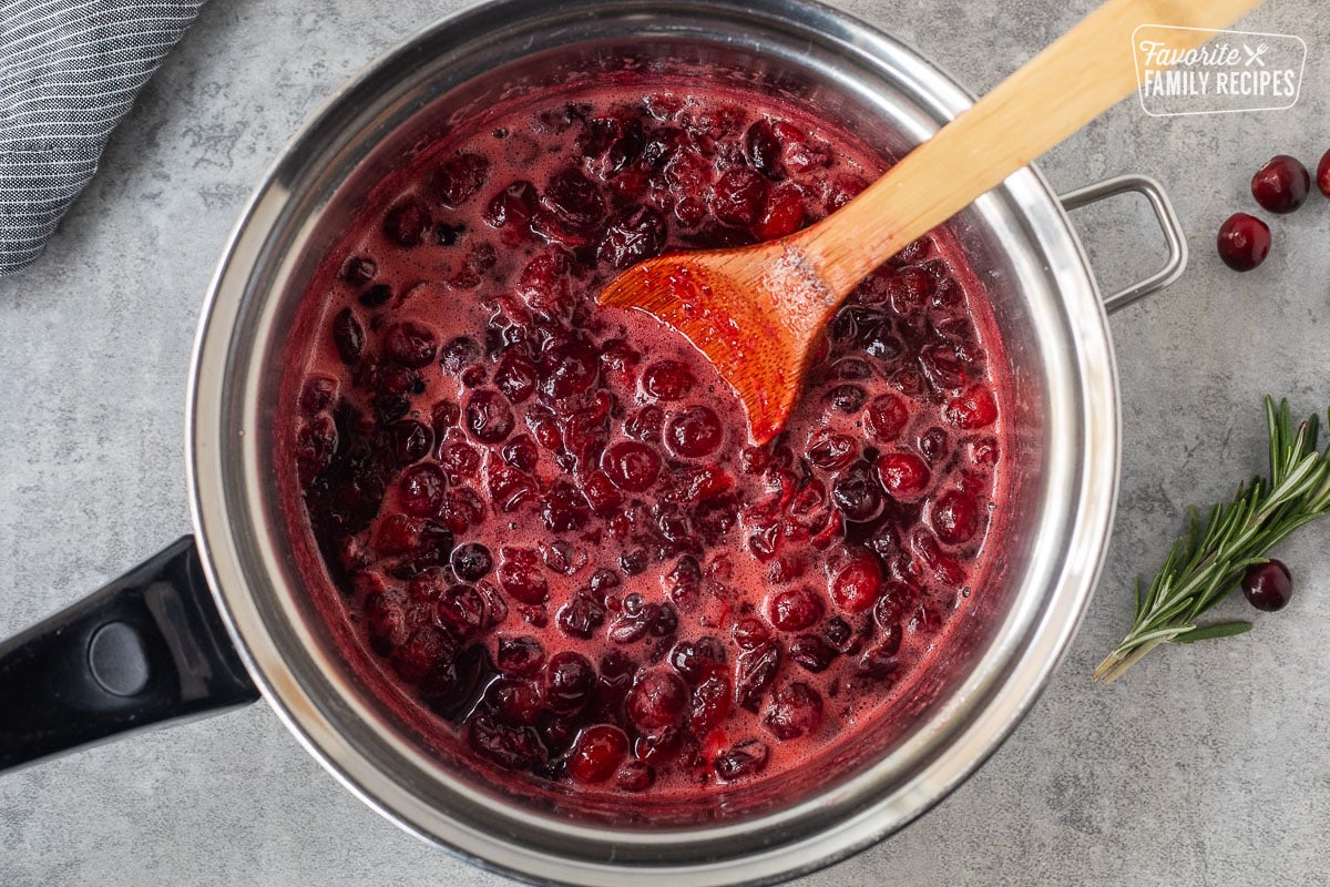 Cranberries cooking in a sauce pan with a wooden spoon.