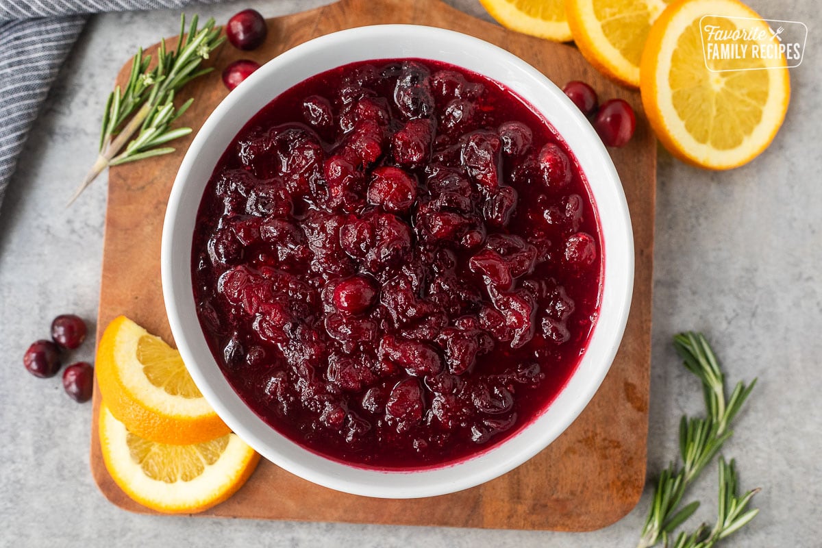 Orange cranberry sauce in a bowl on a board with fresh cranberries, and orange slices on the side.