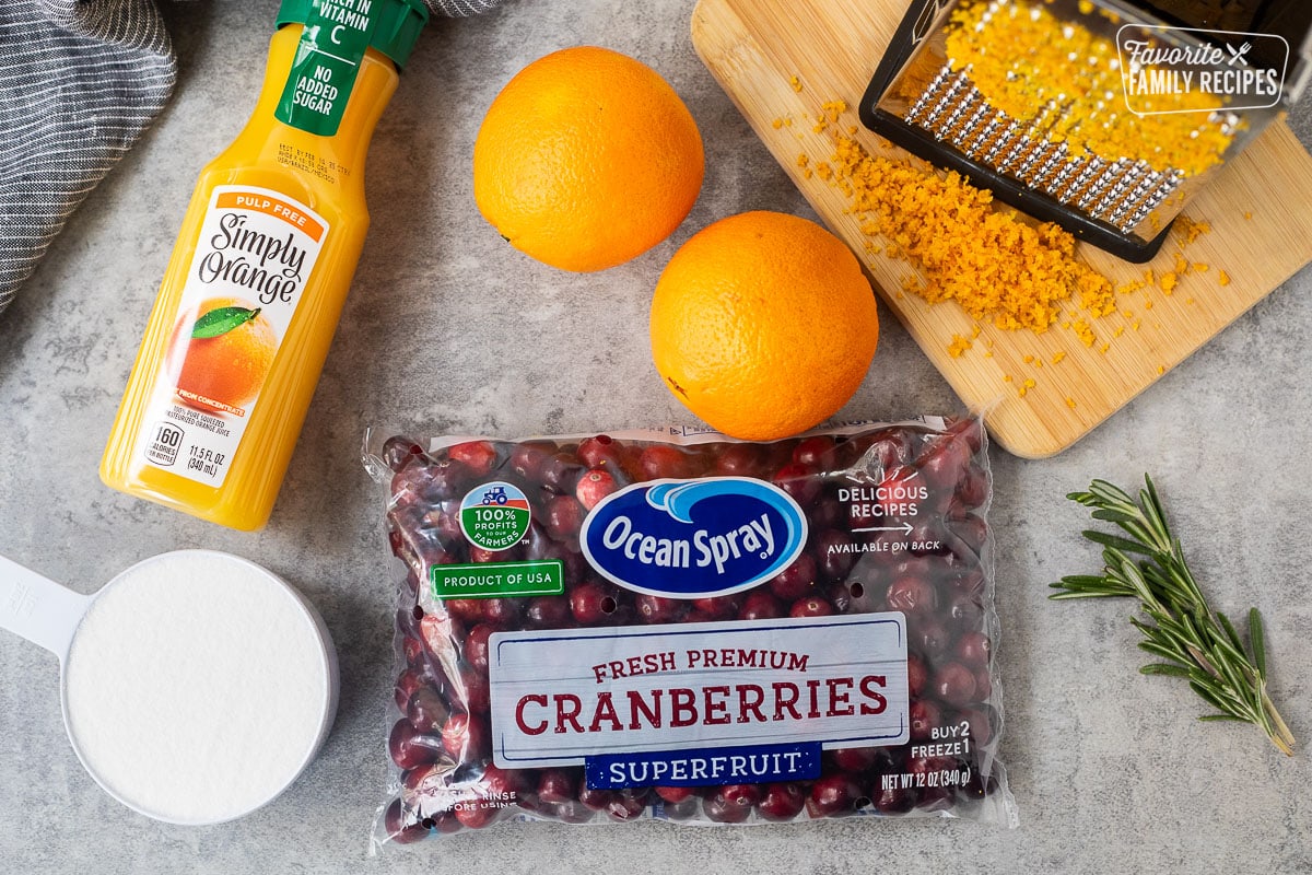 Ingredients to make homemade orange, cranberry sauce, including fresh cranberries, orange zest, orange juice and sugar. Rosemary on the side for garnish.