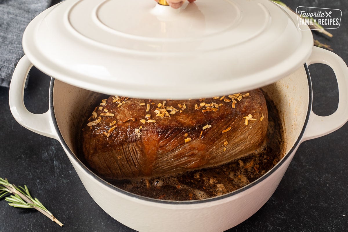 Placing lid on dutch oven with browned oven roast beef.