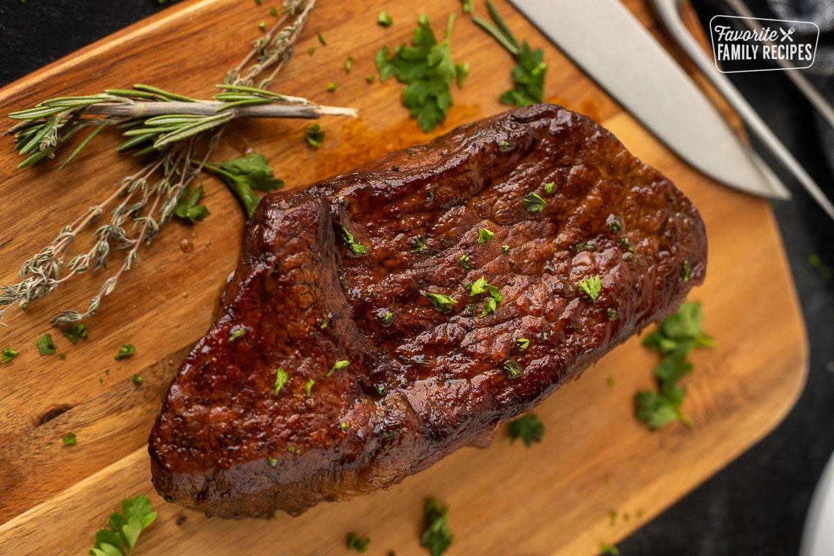 Oven roast beef on a cutting board topped with fresh herbs.