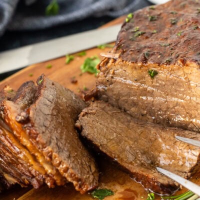 Fork in piece of oven roast beef on a cutting board.