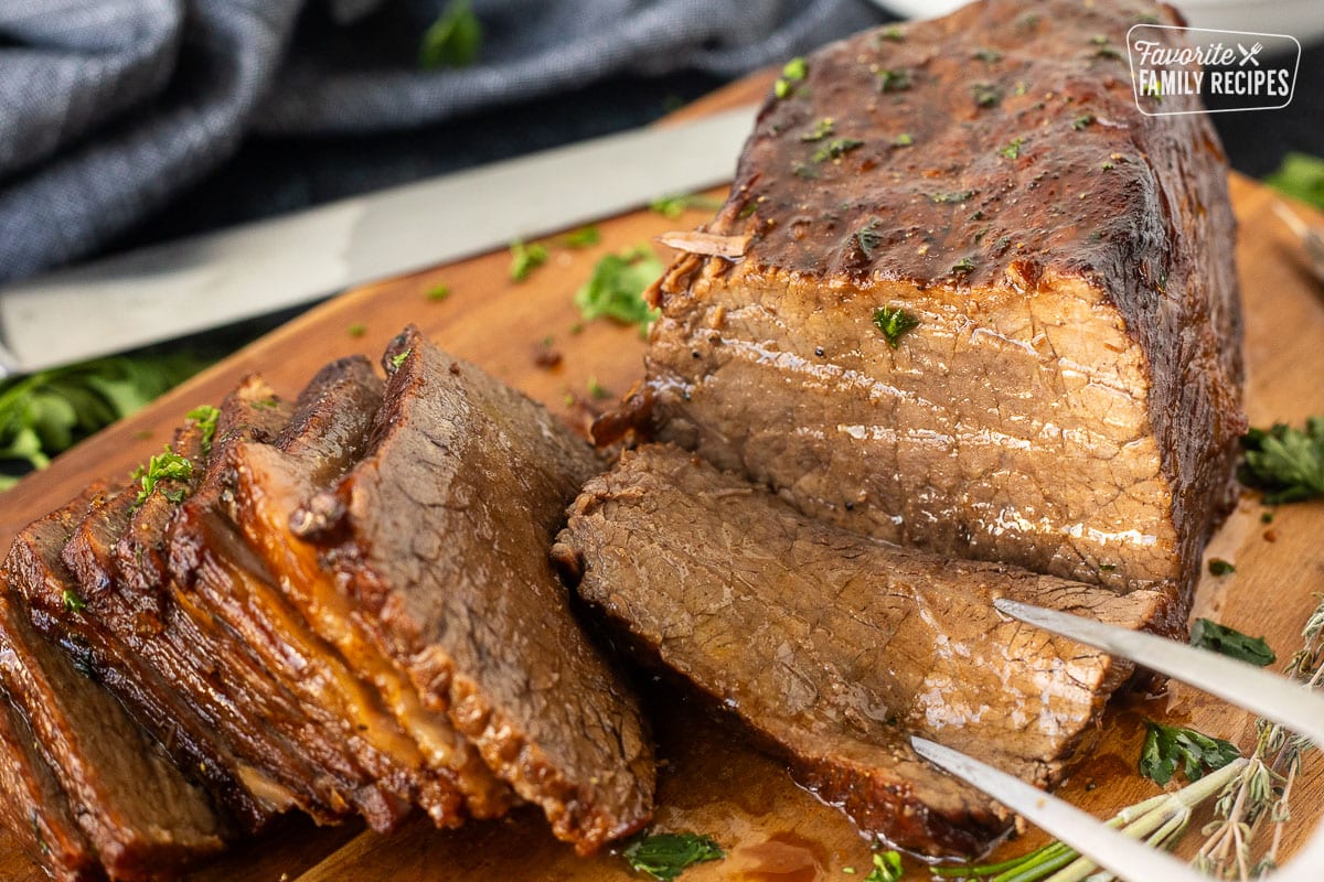 Fork in piece of oven roast beef on a cutting board.