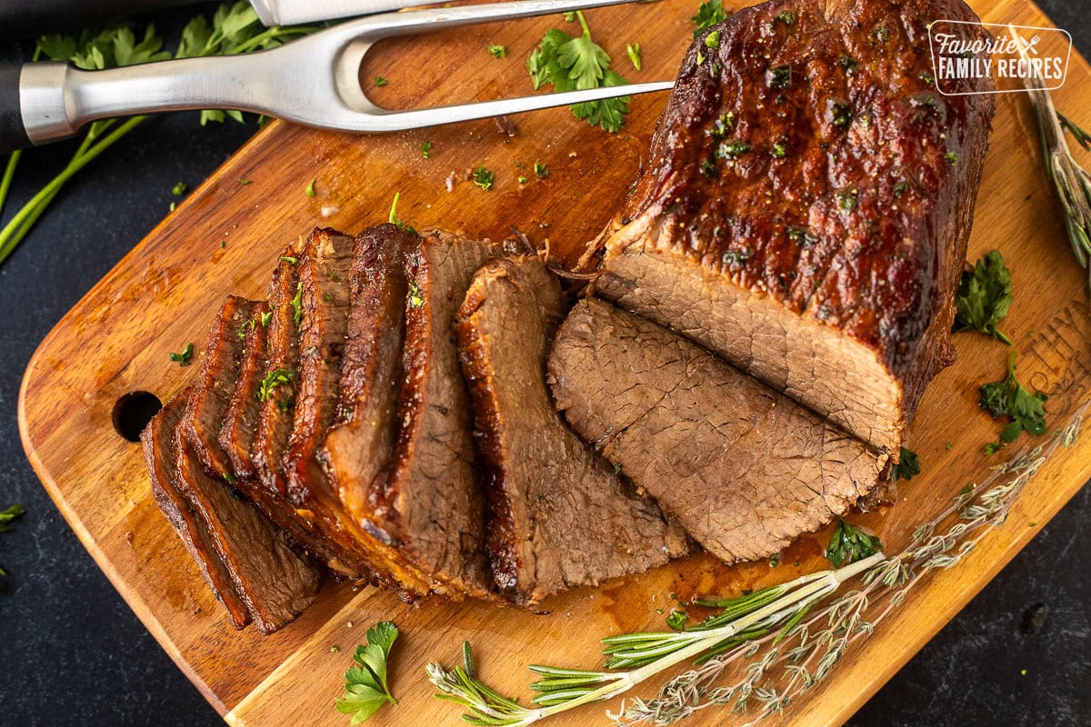 Cutting board with sliced oven roast beef garnished with fresh herbs.