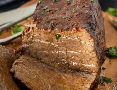 Sliced oven roast beef on a cutting board with fresh herbs.