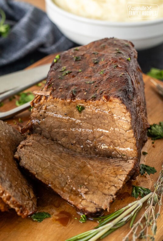 Sliced oven roast beef on a cutting board with fresh herbs.