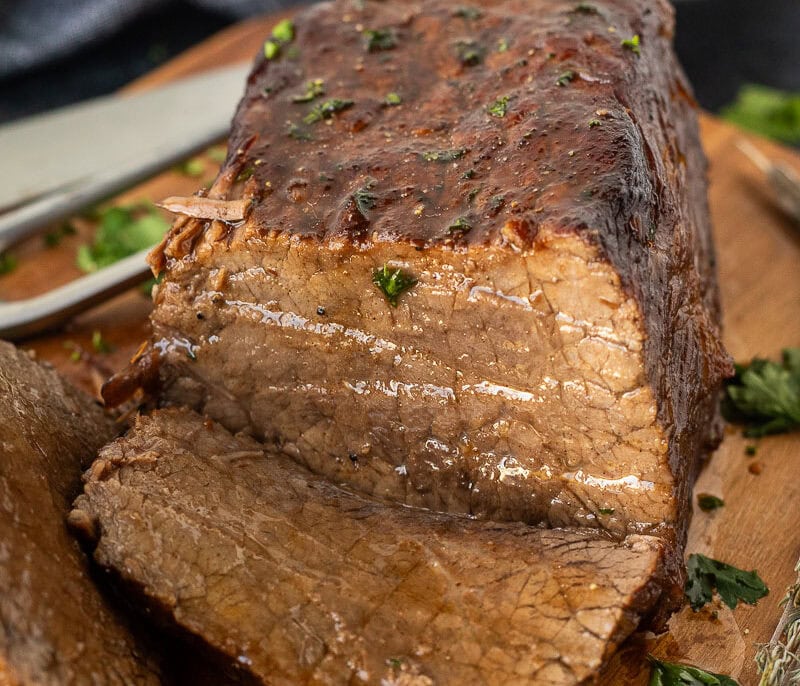 Sliced oven roast beef on a cutting board with fresh herbs.