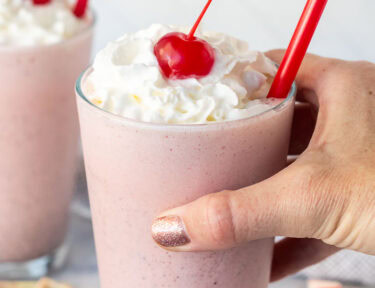 Hand holding a glass with Chick Fil A Peppermint Milkshake topped with whipped cream and a cherry.