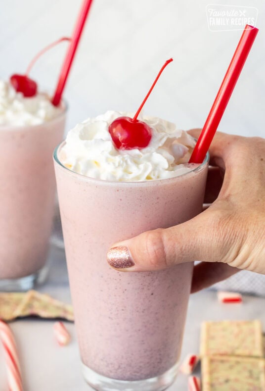 Hand holding a glass with Chick Fil A Peppermint Milkshake topped with whipped cream and a cherry.