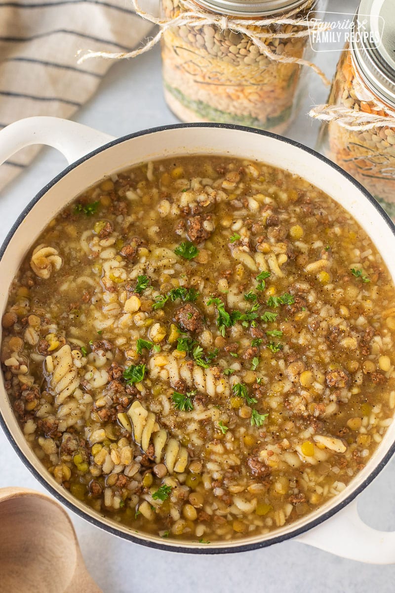 Pot of soup with ground beef, lentils and pasta. Two mason jars of dry soup ingredients on the side.