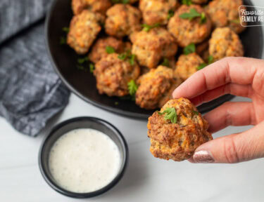 Hand holding a Red Lobster Sausage Ball. Cup of Ranch on the side.