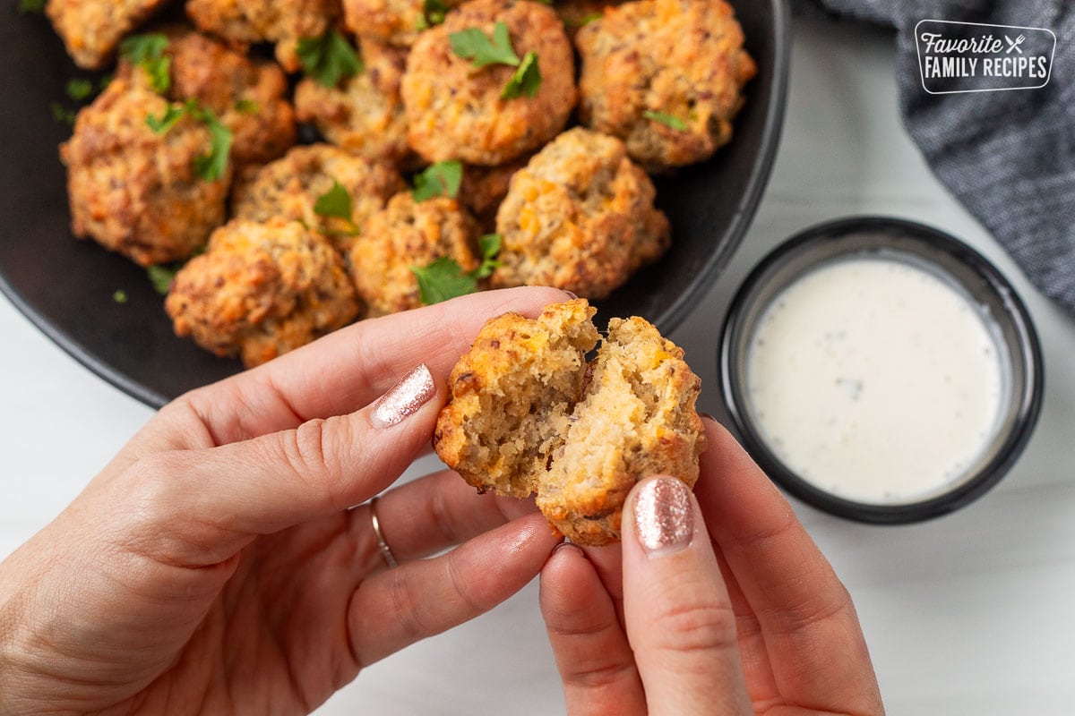 Hands pulling apart a Red Lobster Sausage Ball. Cup of ranch and bowl of sausage balls on the side.