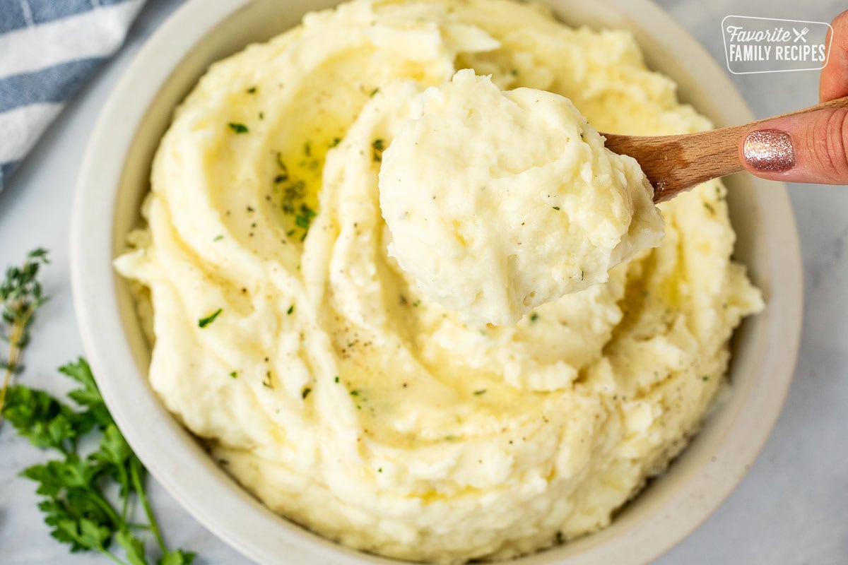 Wooden spoon lifting a scoop of creamy mashed potatoes.