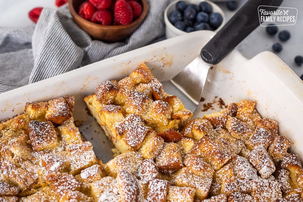 Spatula under a slice of brioche French toast casserole in a baking dish.