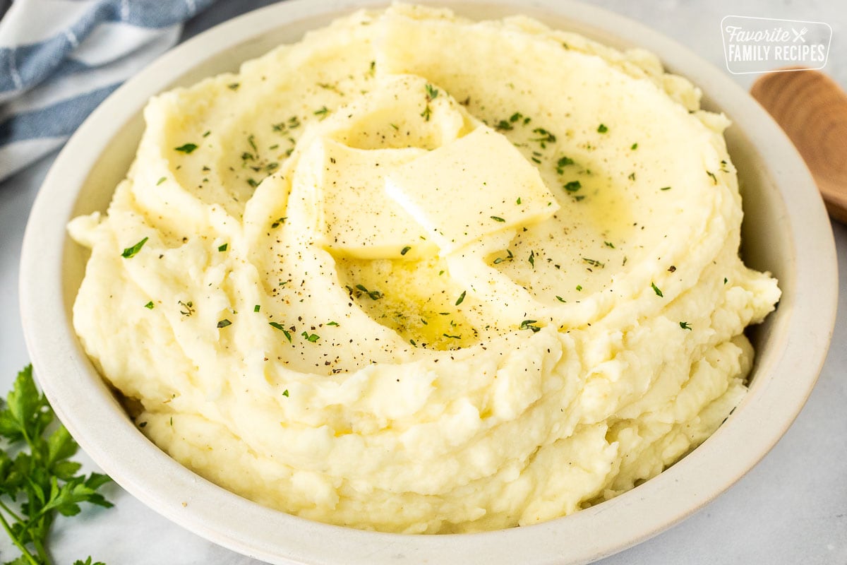 Bowl of mashed potatoes with fresh herbs, pepper, and butter.