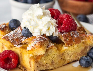 Plate with brioche French toast casserole, fresh blueberries, and raspberries and syrup.