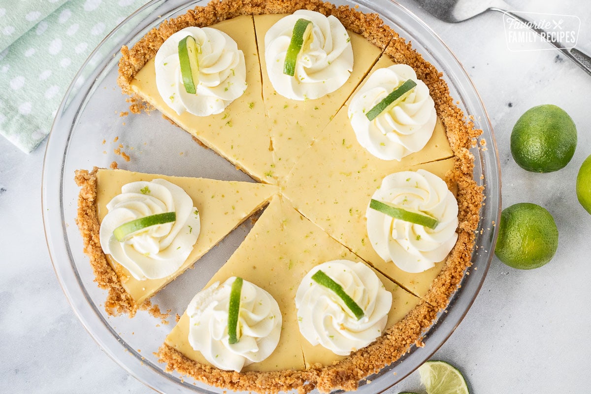 A beautifully decorated whole key lime pie with one slice removed.