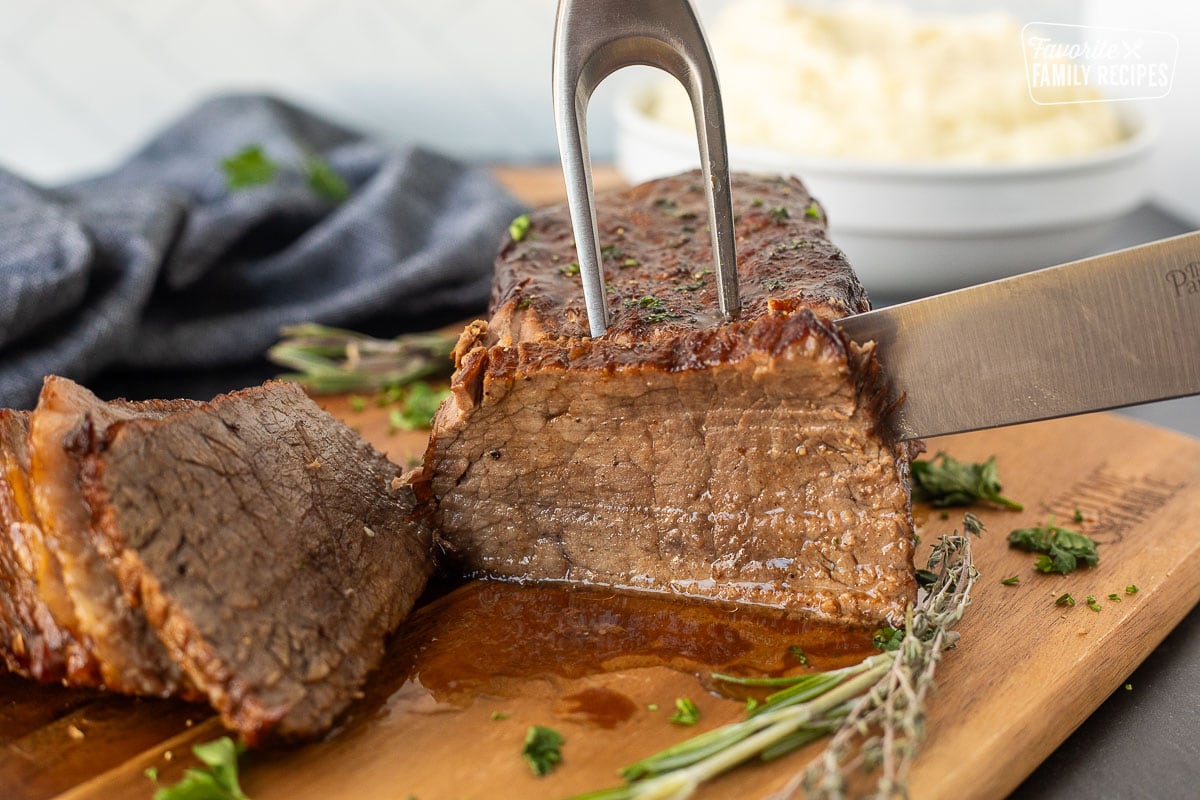 Cutting oven roast beef with a knife and carving fork.