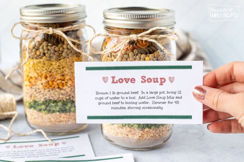 Hand holding up a Love Soup label with two mason jars with dry soup ingredients.