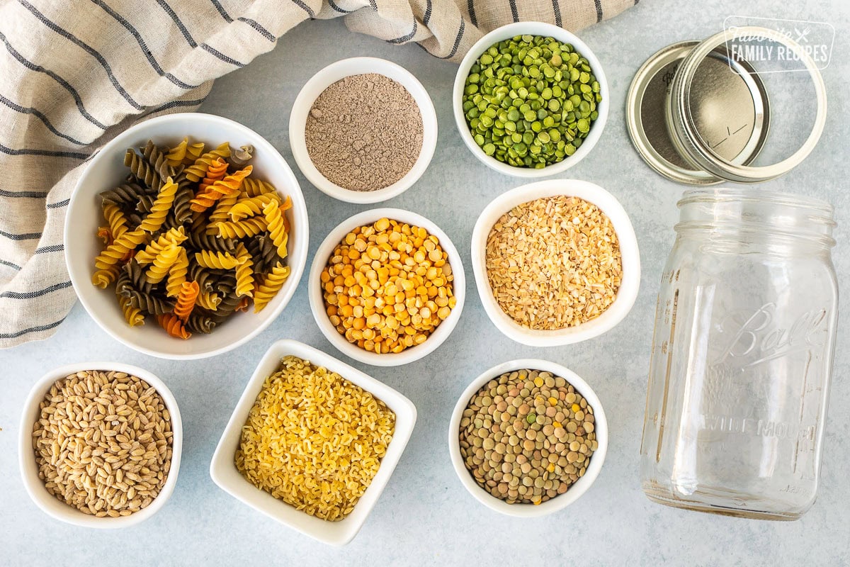 Ingredients to make Soup in a Jar including a quart sized jar with lid, dried onion, split green peas, split yellow peas, lentils, barley, alphabet pasta, beef bouillon and tri-colored pasta.