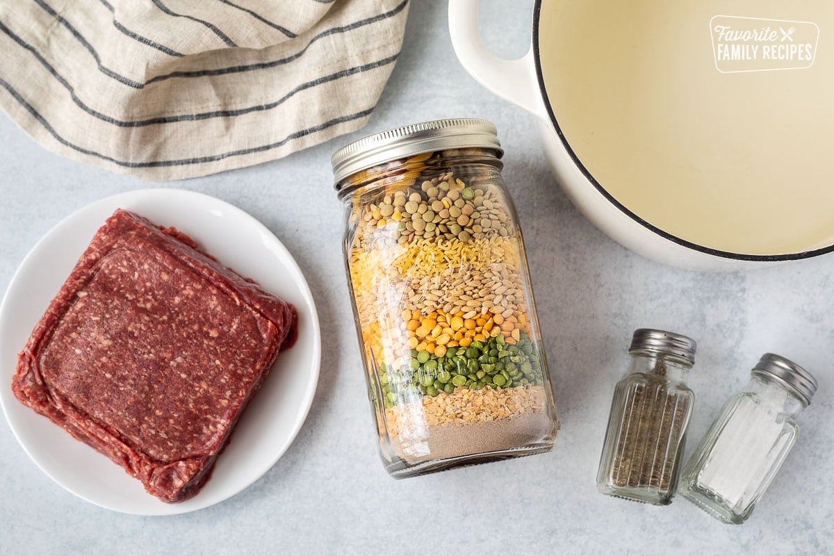 Ingredients to make soup including pot of water, soup in a jar, salt, pepper and ground beef.