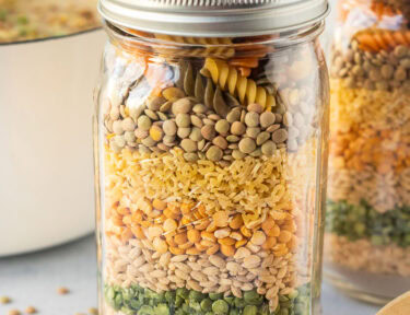 Two jars of dry ingredients for soup next to pot of soup and ladle.