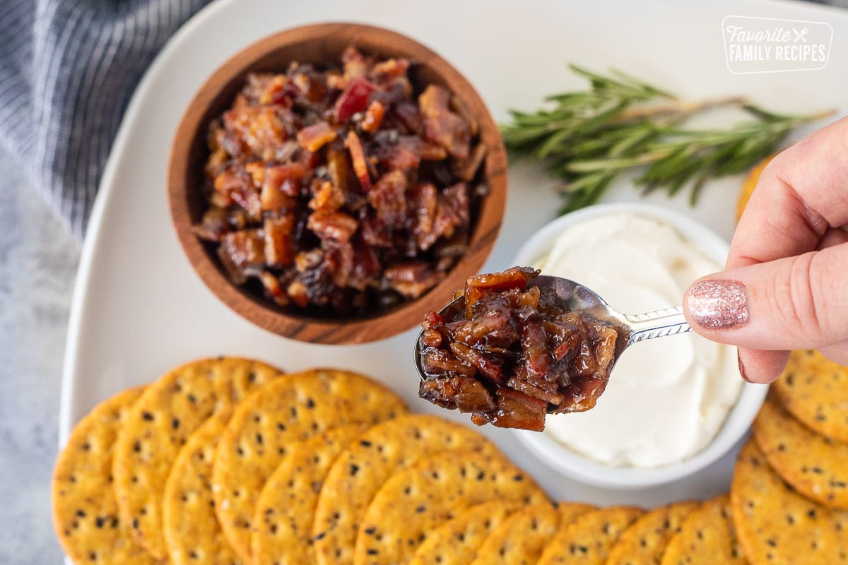 Spoon of bacon jam over a plate of crackers and cream cheese