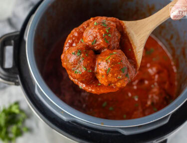 Wooden spoon holding up three instant pot meatballs.