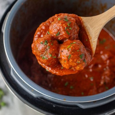 Wooden spoon holding up three instant pot meatballs.