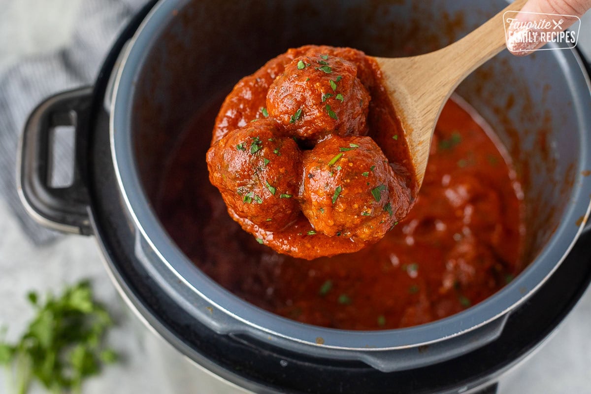 Wooden spoon holding up three instant pot meatballs.