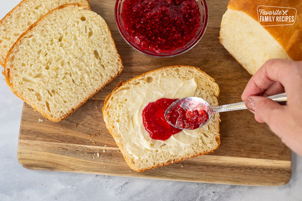 Spreading raspberry jam on a slice of buttered bread.