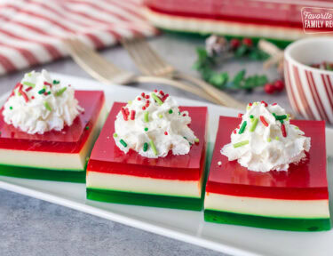 Three slices of Christmas Jell-O salad on a plate with whipped cream and sprinkles.